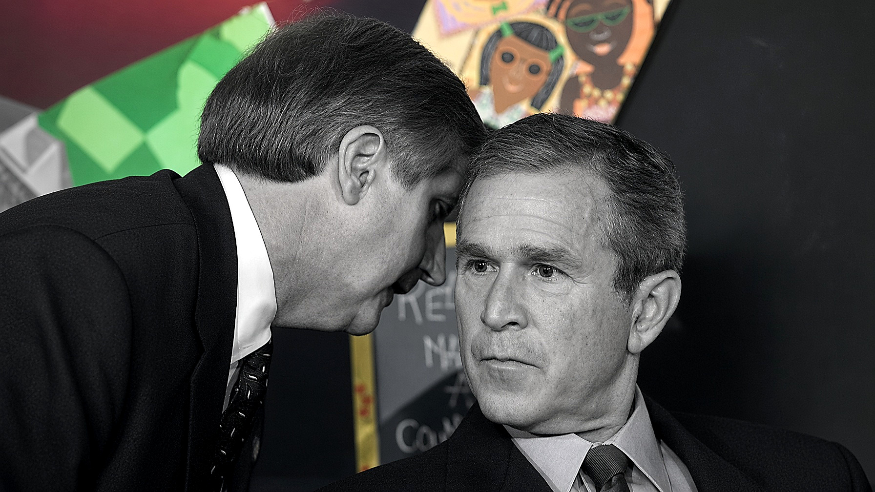 Chief of Staff Andrew Card whispers to President George W. Bush in a Sarasota classroom on Sept. 11, 2001: both figures in black and white; children’s mural and chalkboard in color. Editor’s plate.