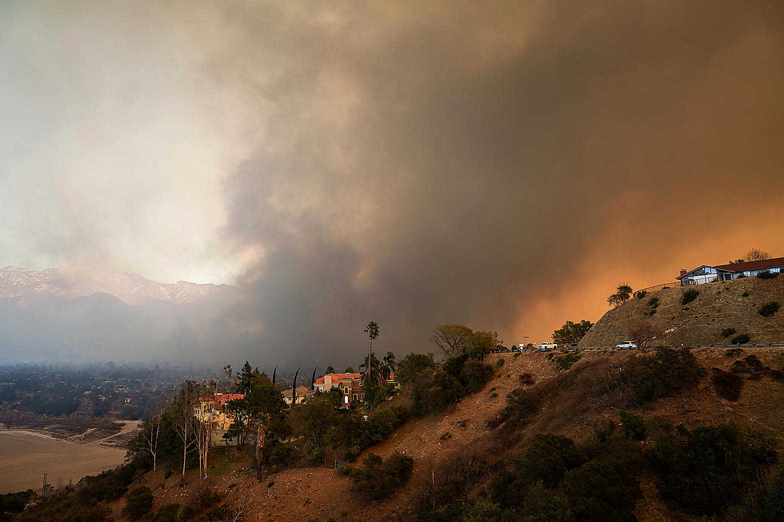 A California hillside under a brown column of wildfire smoke, houses on a ridge, sky and brush in color. No figures in the frame.
