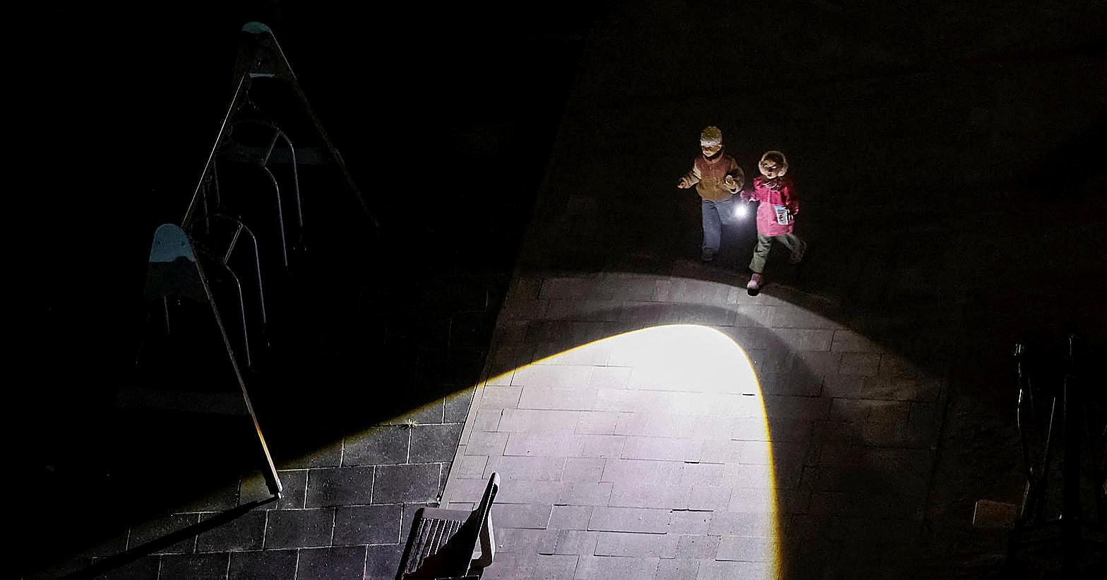 Two children cross a dark playground with a flashlight after Russian strikes cut power in Ukraine.