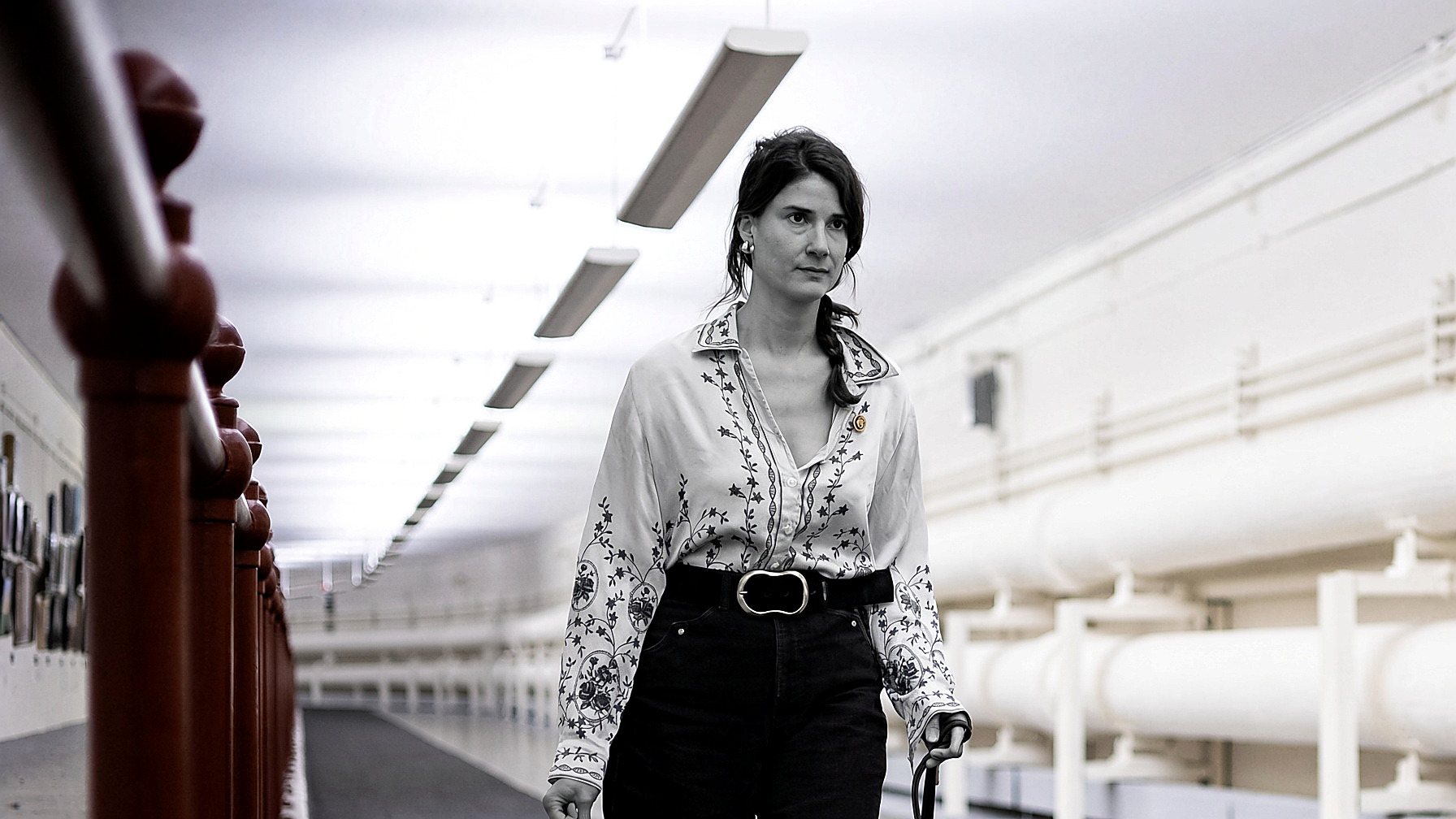 Rep. Marie Gluesenkamp Perez walking a Capitol hallway: the figure in black and white; railing, pipes and ceiling in color. Wire photograph.