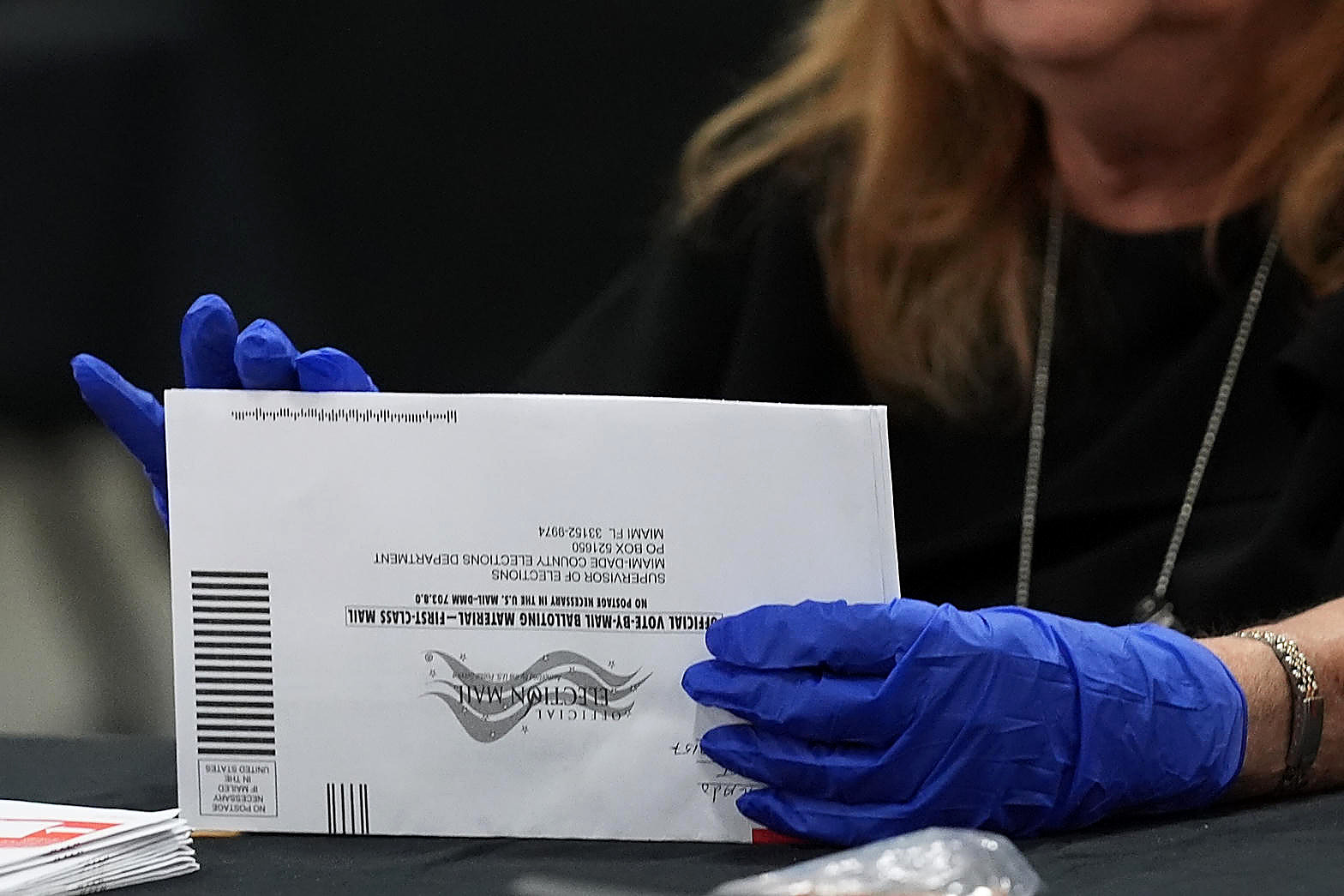 A mail ballot envelope in gloved hands, full color. Wire photograph.