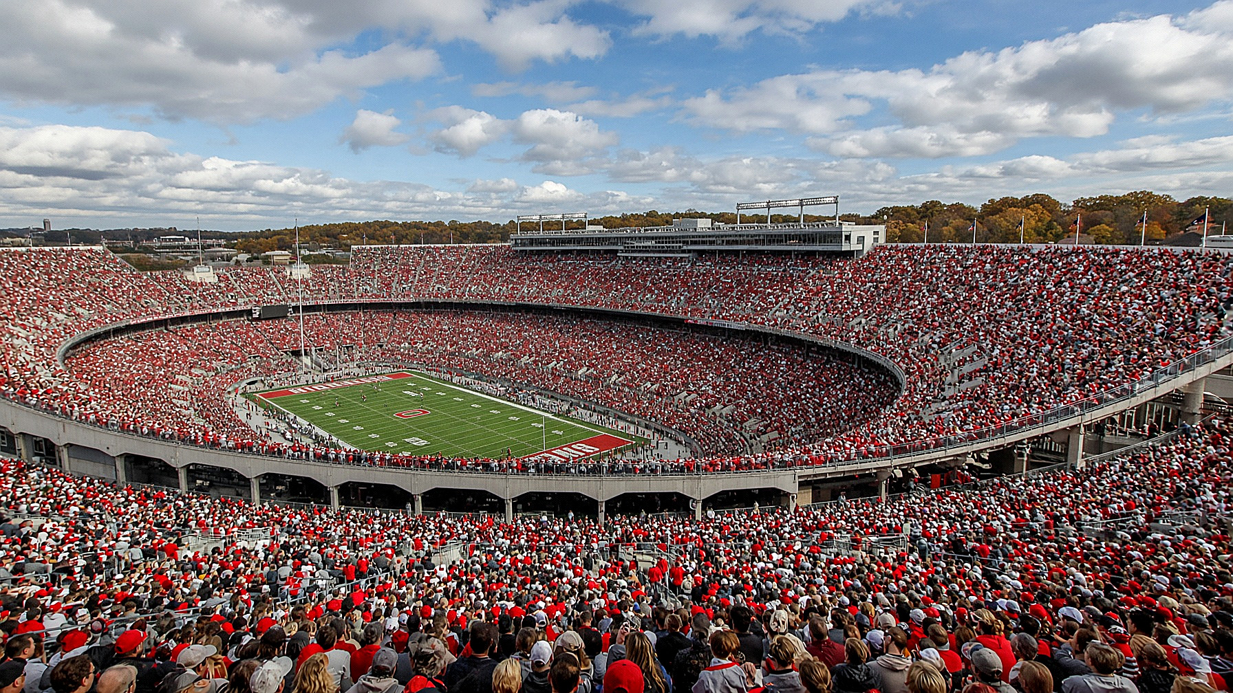 Ohio Stadium, the Horseshoe packed in scarlet and gray, field below, in color. Crowd as texture. No identifiable faces.