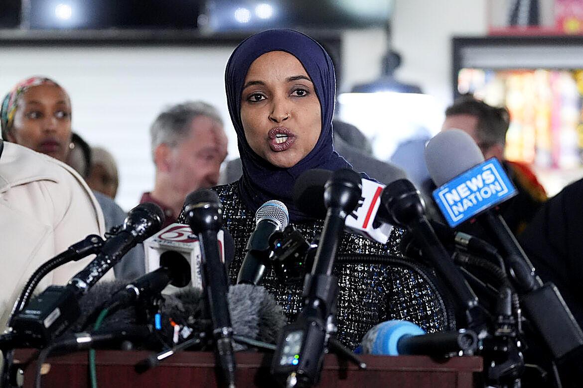 Representative Ilhan Omar, speaking into a bank of microphones, said she will not be silenced after agents searched her home.