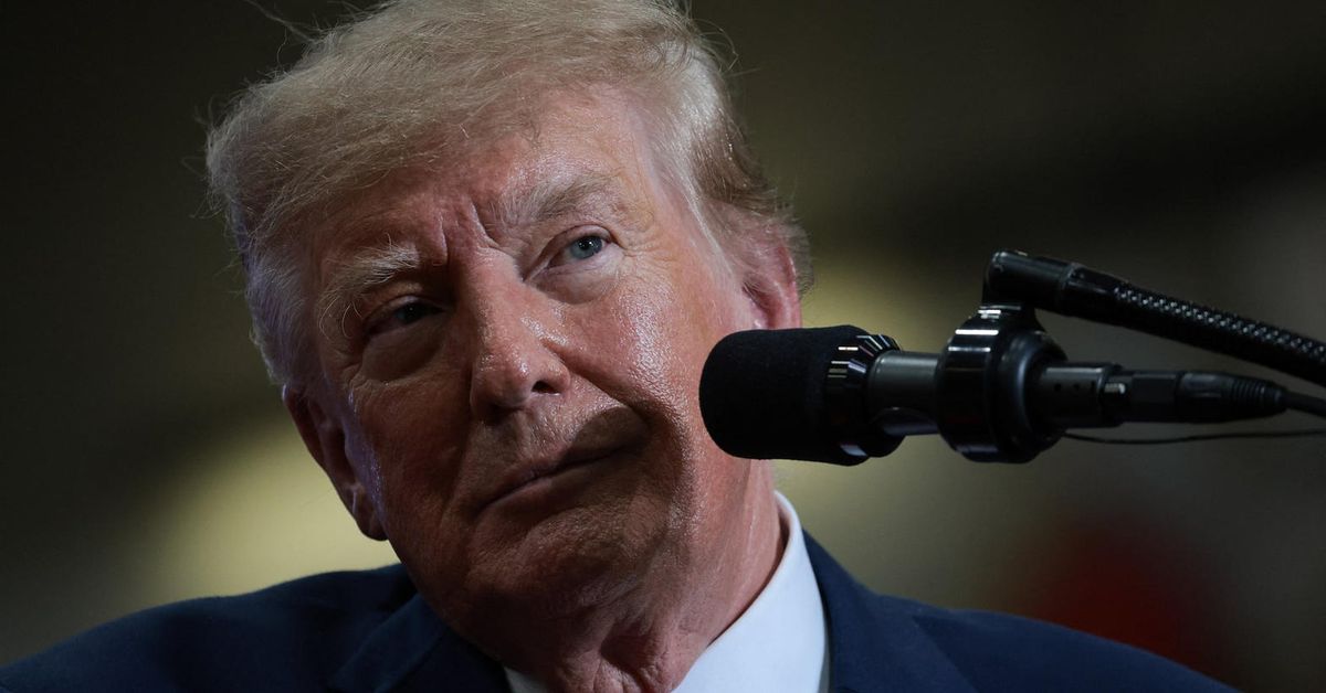 President Trump, in a navy suit and white shirt, speaks into a black microphone at a rally in Port Huron.