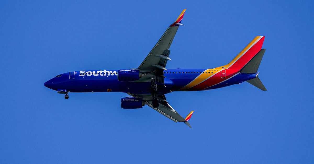 A Southwest jet, blue with a red and gold tail, flies with the landing gear down against a clear sky.