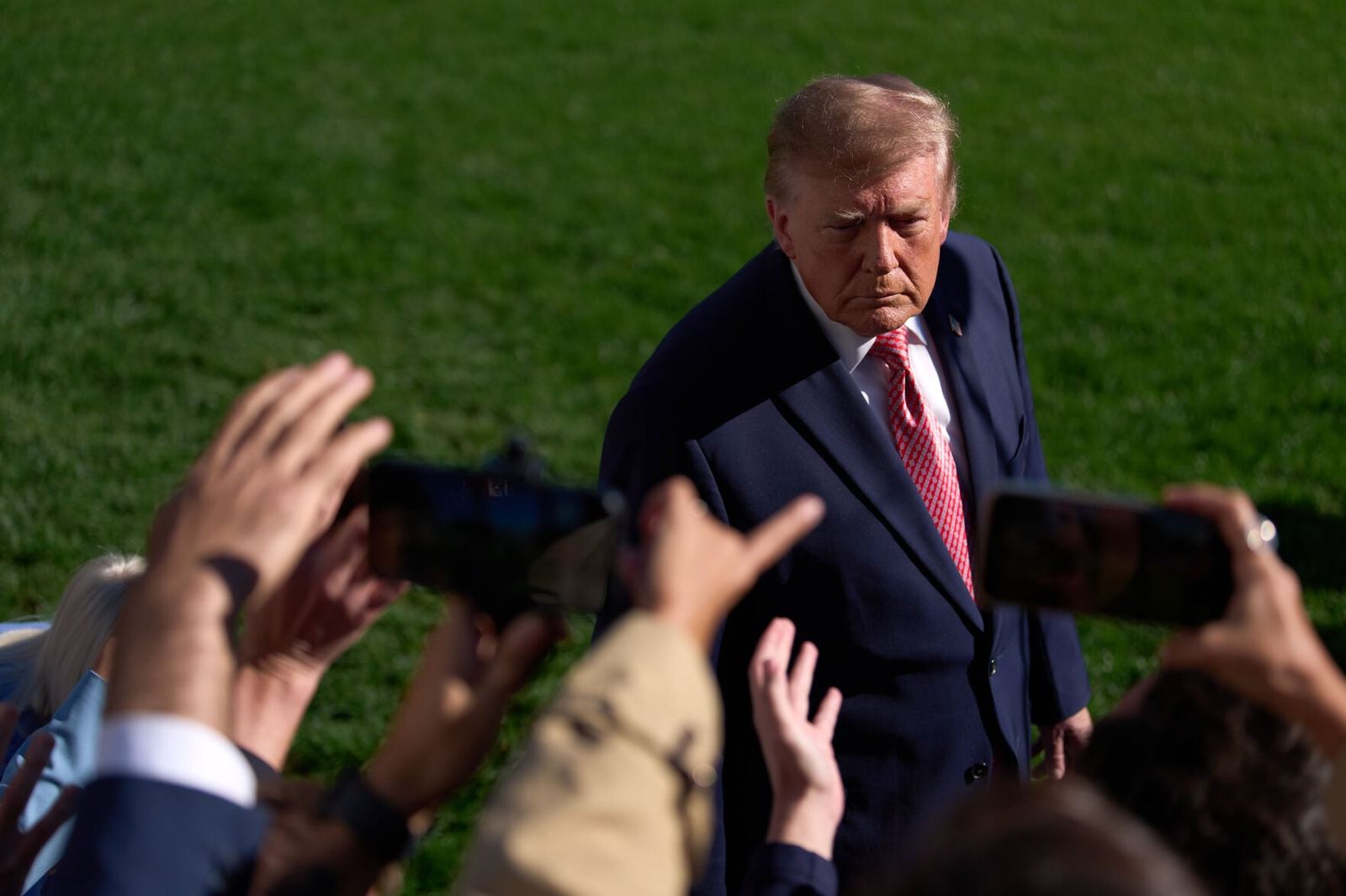 President Trump speaks to reporters on the South Lawn, one hand raised, Marine One behind him.