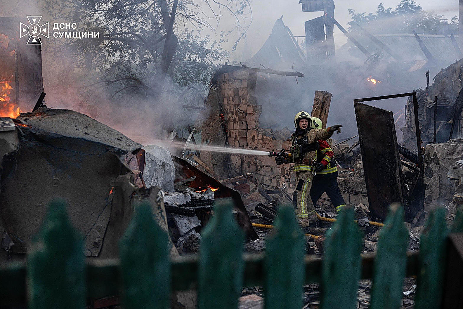 Ukrainian rescuers hose a burning house after a strike, rubble and smoke, in color. Wire photograph.