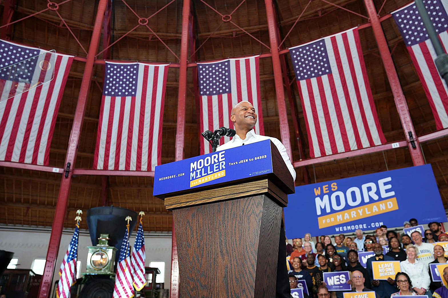 Maryland Gov. Wes Moore at a podium, flags behind him, in color. Person plate.