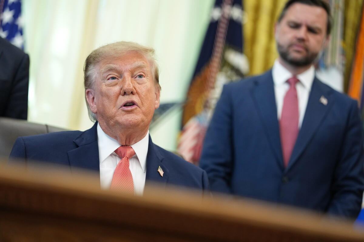 President Trump speaks in the Oval Office, mouth open, a red striped tie, Vice President Vance standing behind him.